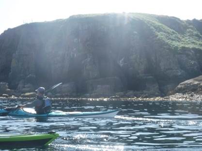 A person in a kayak in the water by a large rock

Description automatically generated with low confidence