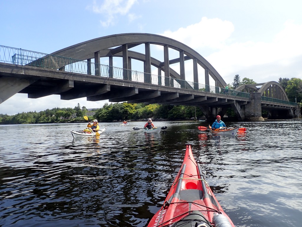 A group of people kayaking under a bridge

Description automatically generated