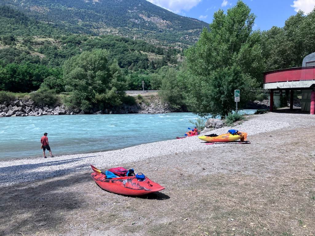 A group of kayaks on a beach next to a river
Description automatically generated