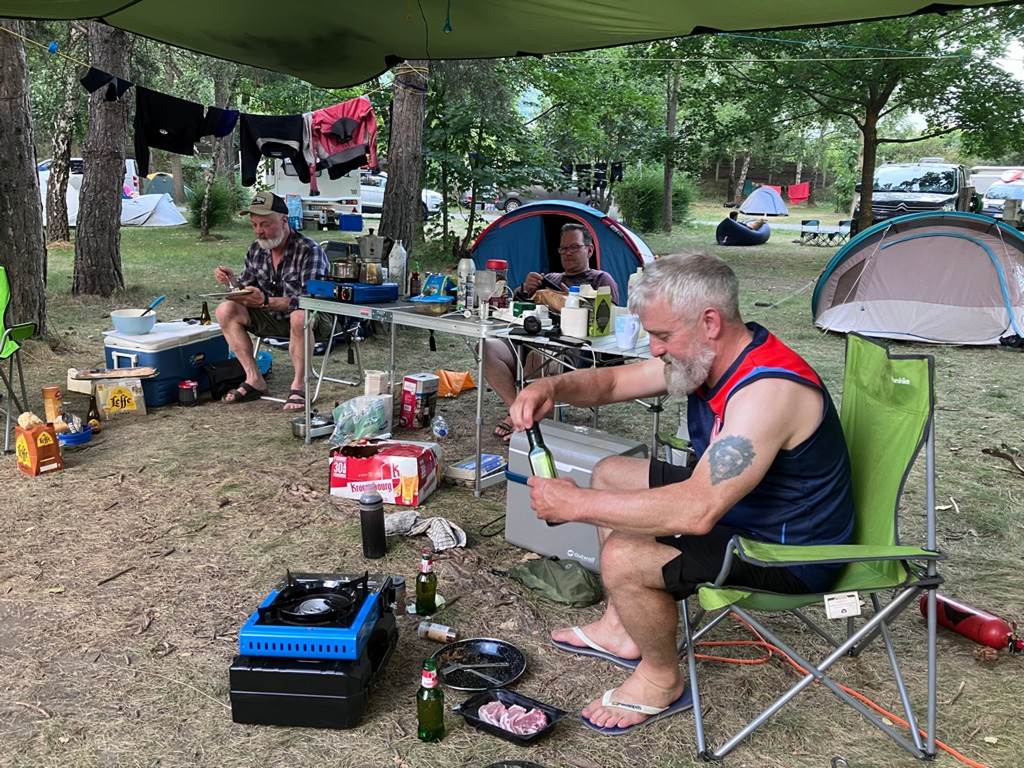 A group of men sitting outside by a table with food and drinks
Description automatically generated