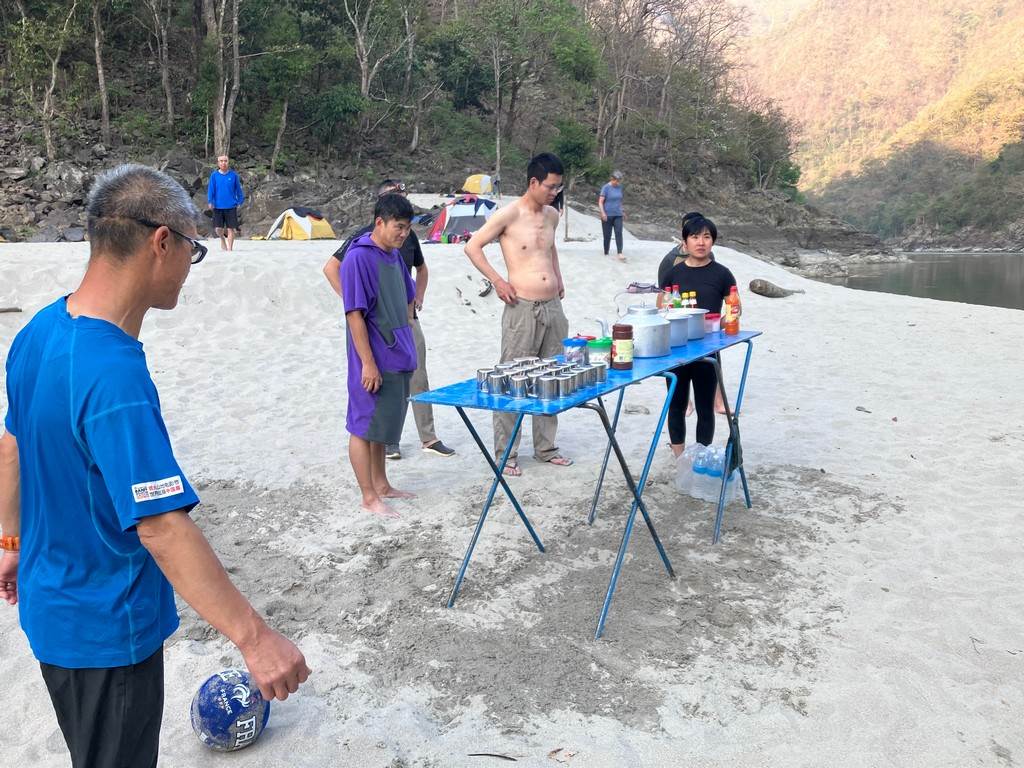 A group of people standing around a table on a beach

Description automatically generated