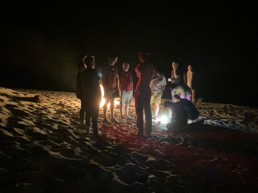 A group of people standing around a fire on a beach

Description automatically generated